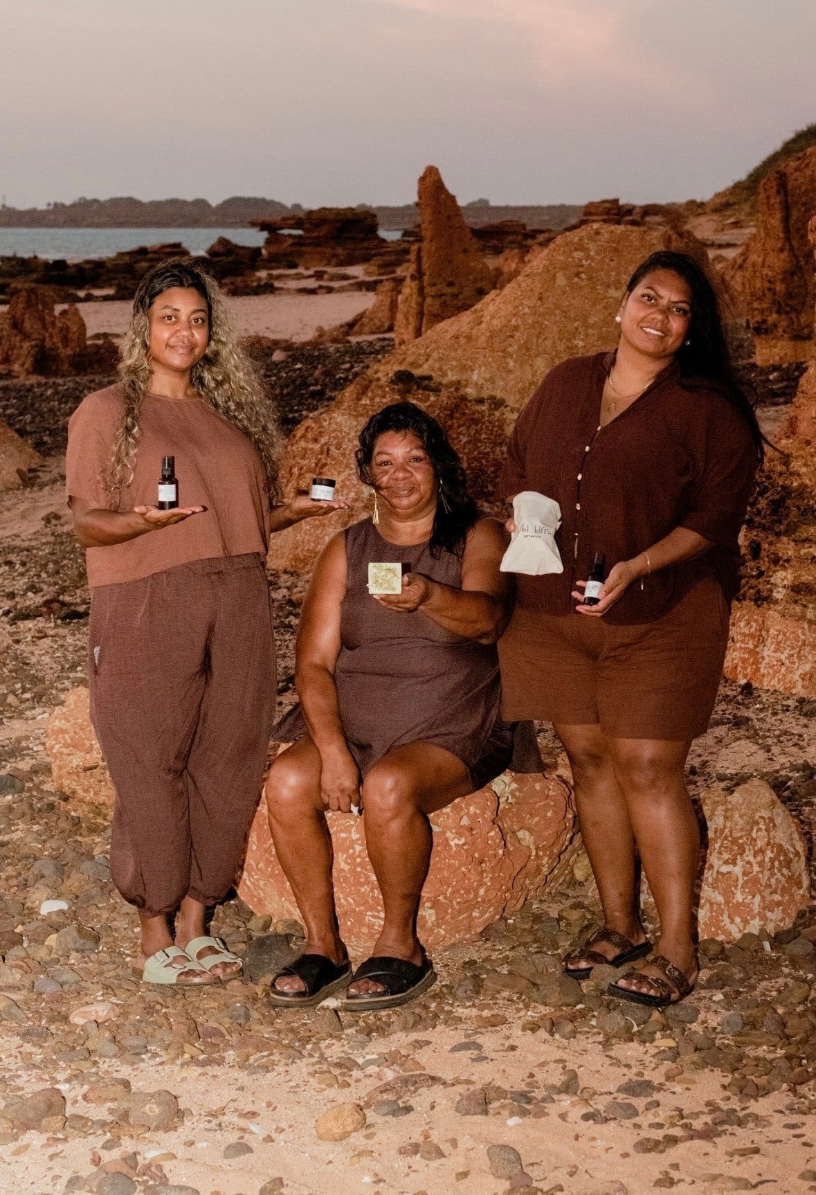 Three family members holding Bibi Birra Botanics products on the coastline