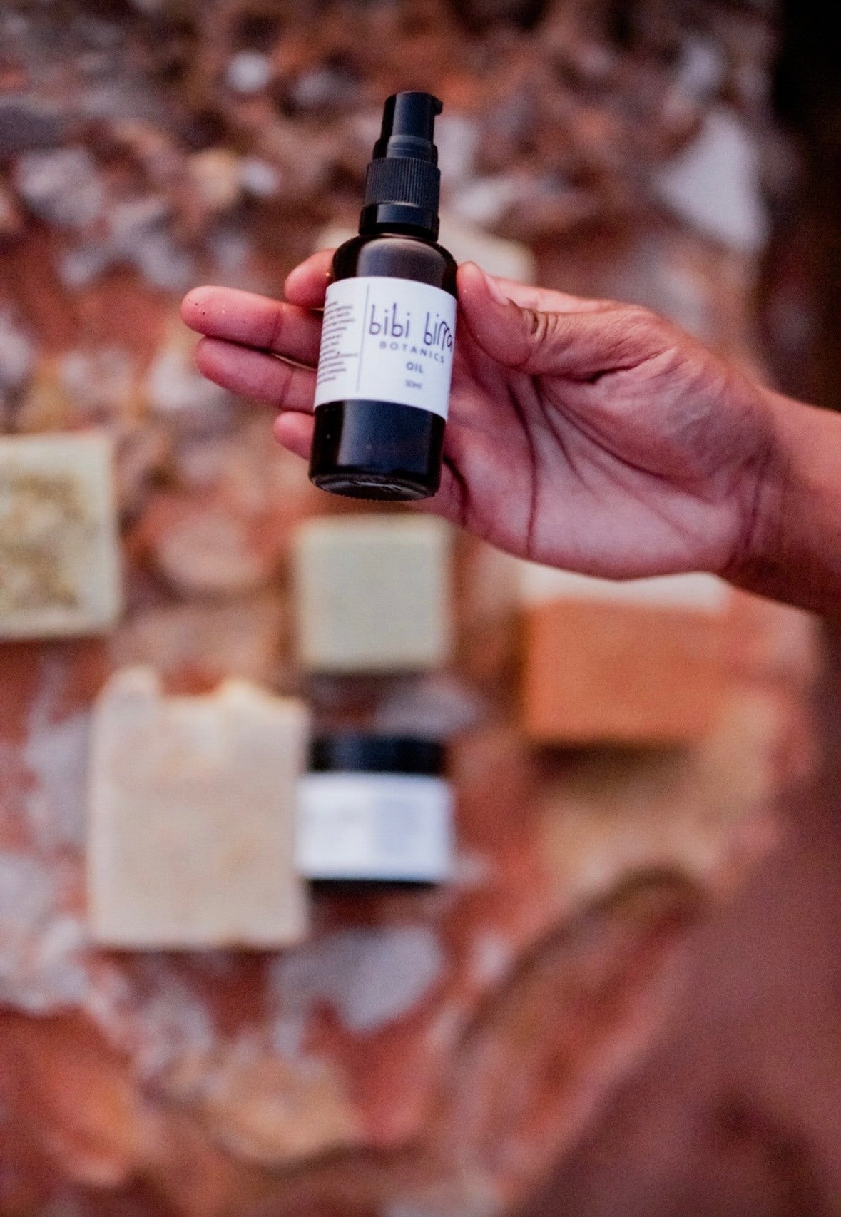 Bibi Birra Botanics oil bottle held against coastal rock